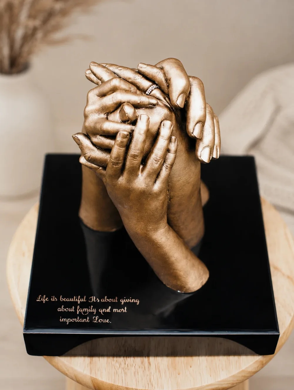 Four hands cast in bronze, holding one another, on a black base engraved Life is beautiful, it's about giving, about family and most important love