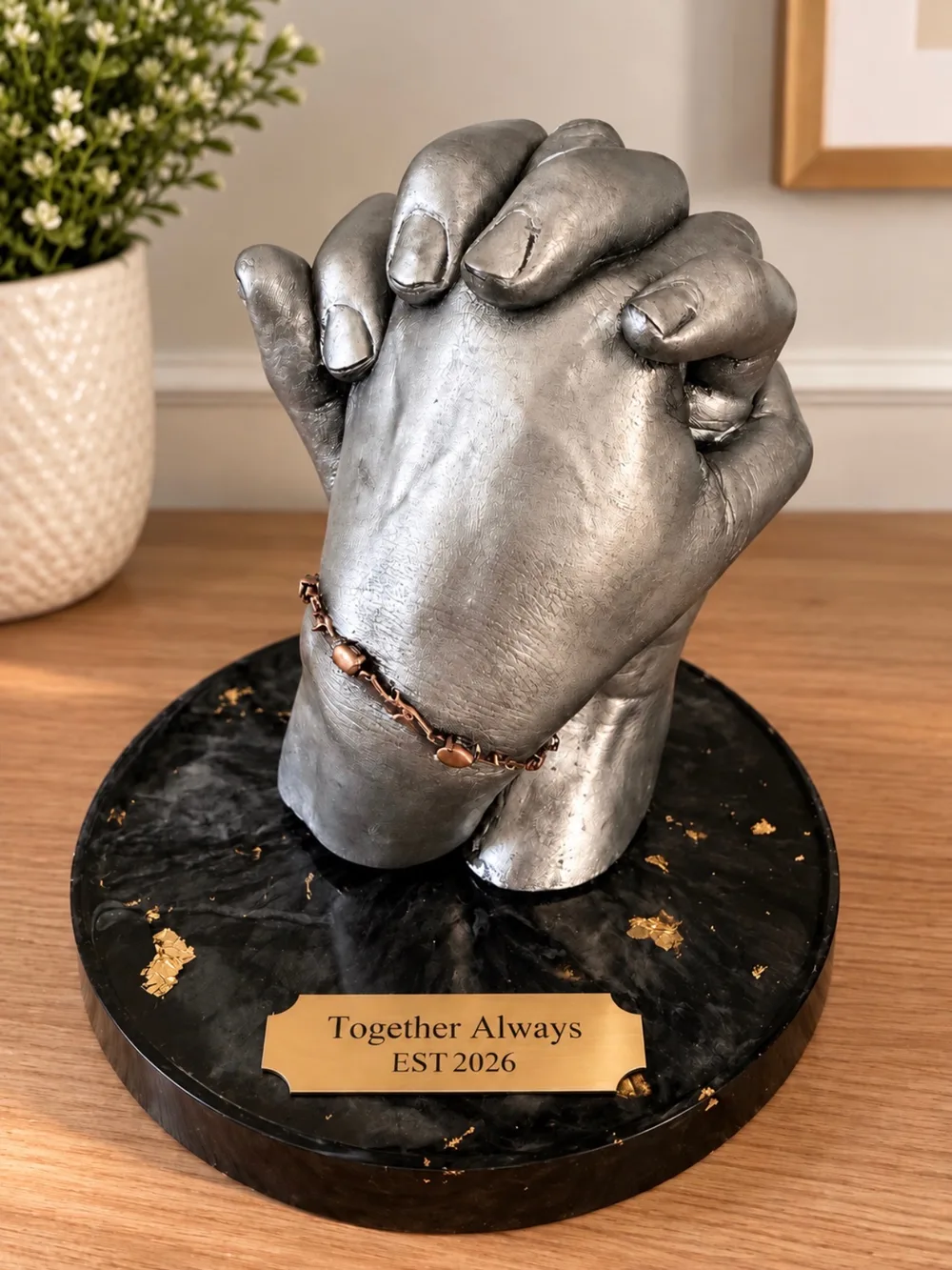Two clasped hands cast in silver with a copper bracelet, on a round black base with gold flakes and a brass plate reading Together Always, EST 2026