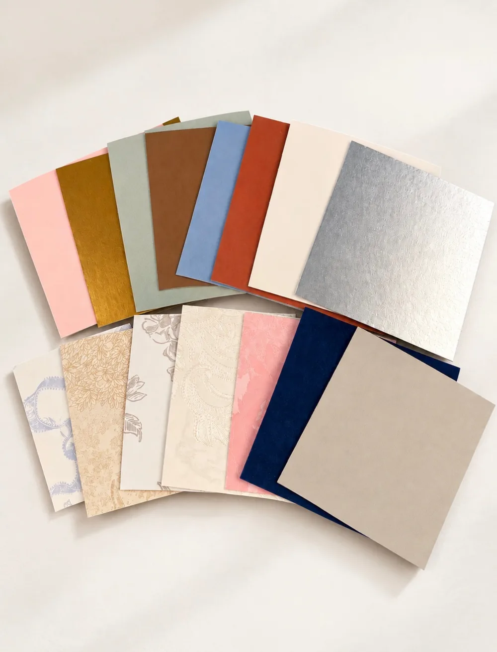 Mat board samples fanned out: blush, gold foil, sage, brown, powder blue, rust, cream, silver foil, navy, taupe and patterned lace, floral and marbled boards