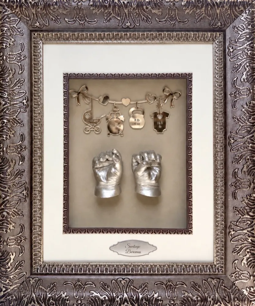3D silver casts of a baby's hands under a row of tiny gold charms, in an ornate bronze frame